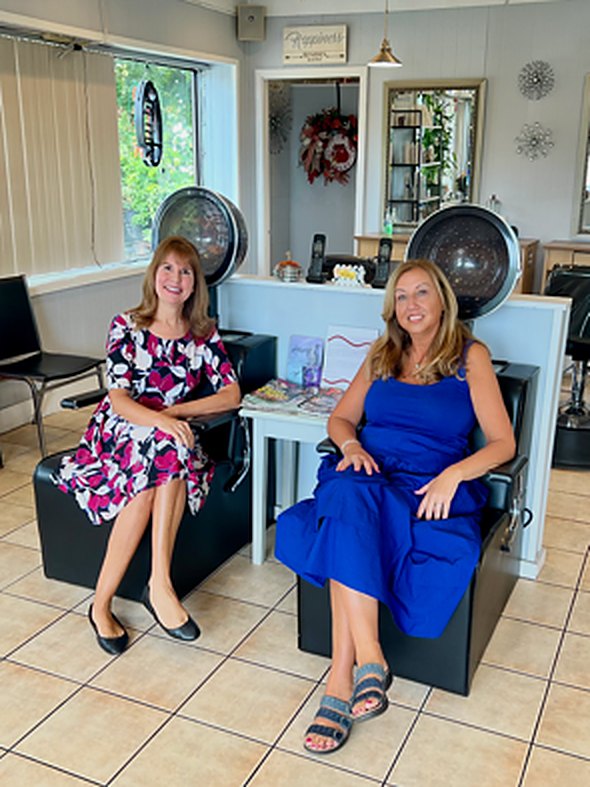 Two women smiling as they sit in salon dryer chairs